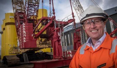 Smiling man at Wilton Engineering stands in front of crane and yellow pillars