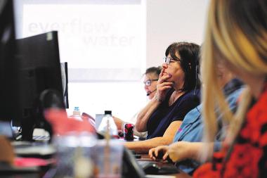 Woman at Everflow looks contemplatively at her computer screen, in front of a projector with Everflow in the background