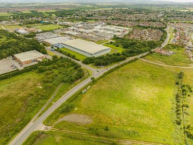 Drone image of site entrance for Durham Lane Industrial Park showing a road with warehouses and green spaces